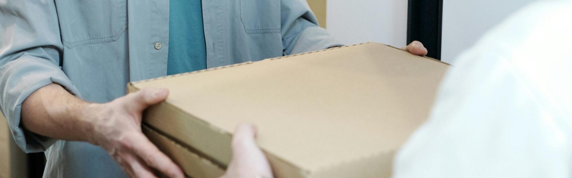 A delivery man with a mask handing over pizza boxes indoors, embodying pandemic safety measures.
